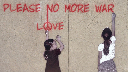 Zwei Mädchen schreiben hoffnungsvoll an eine Mauer: "PLEASE NO MORE WAR - LOVE"